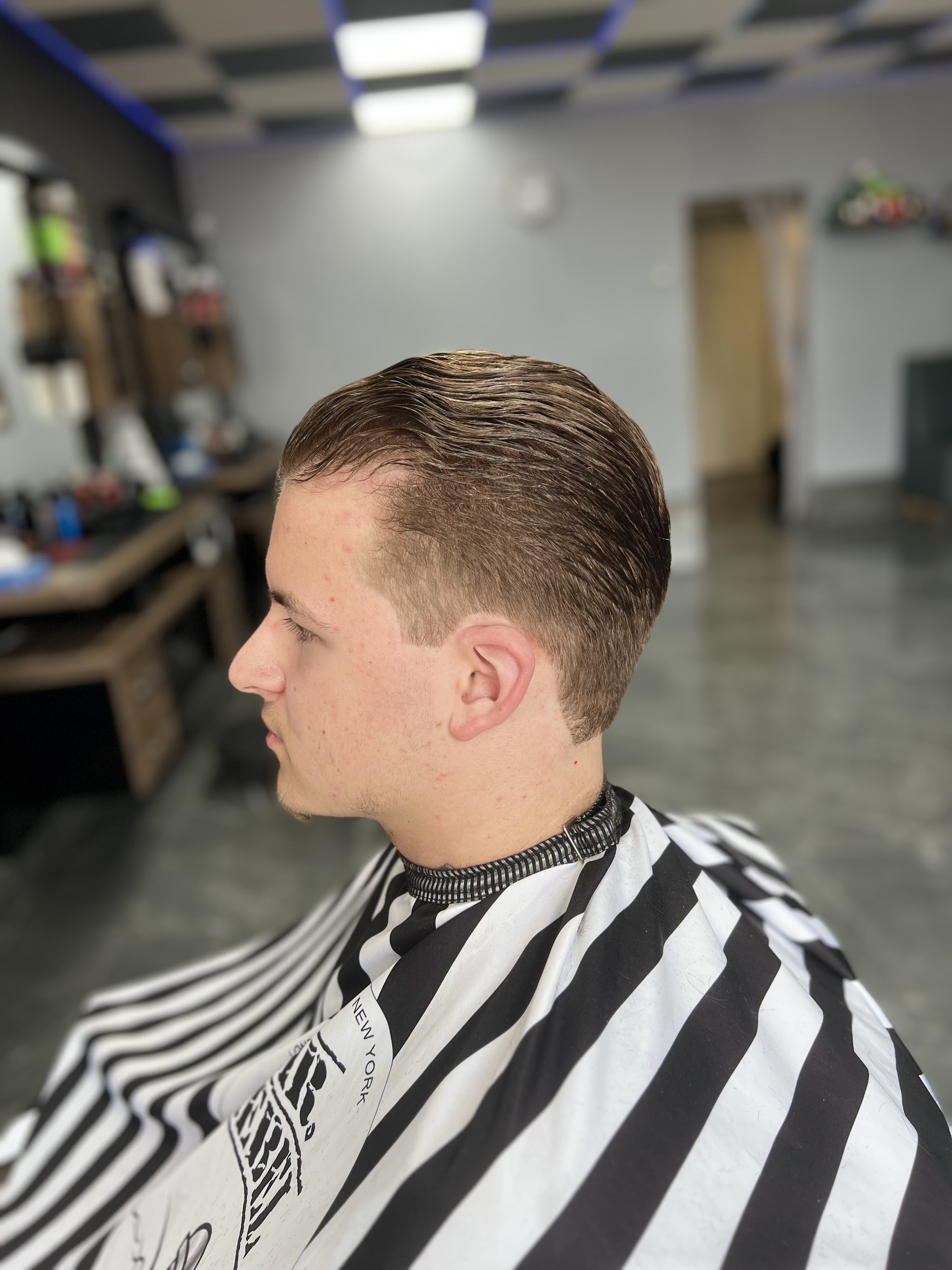 Klant met lang haar bovenop, naar achteren gekamd, in een gestreepte kapmantel in de zaak